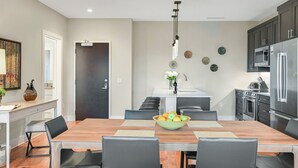 A modern kitchen with dark cabinets, a stainless steel refrigerator, and a dining area with a wooden table and black chairs. - Luxury Condo, Downtown Asheville (Asheville)