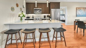 A modern kitchen with a central island, bar stools, stainless steel appliances, and wooden flooring. - Luxury Condo, Downtown Asheville (Asheville)
