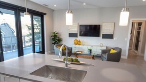 A modern kitchen with a large island, a dining area with a table and chairs, and a living area with a sofa and a TV.
