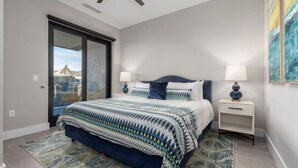 A bedroom with a bed, two bedside tables, a ceiling fan, a large window, and a view of the outside.