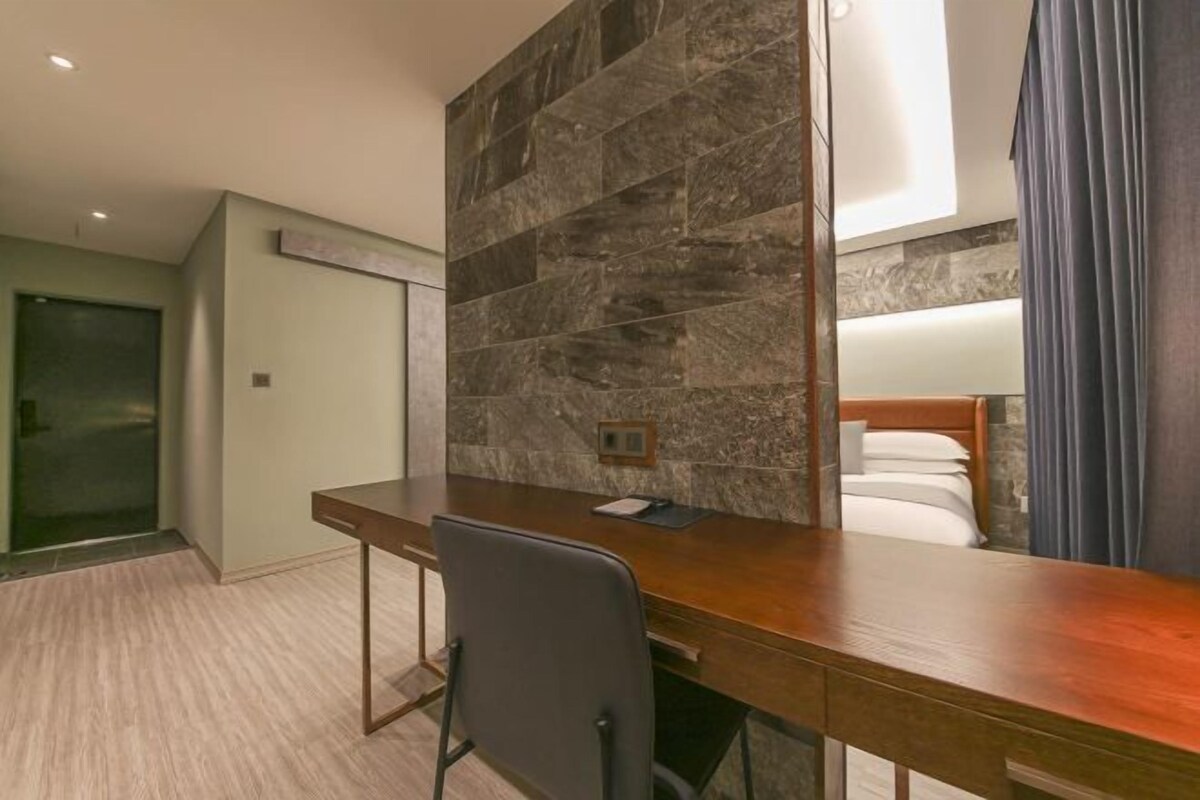 A hotel room with a wooden desk, a chair, a stone accent wall, and a bed with a blue curtain.