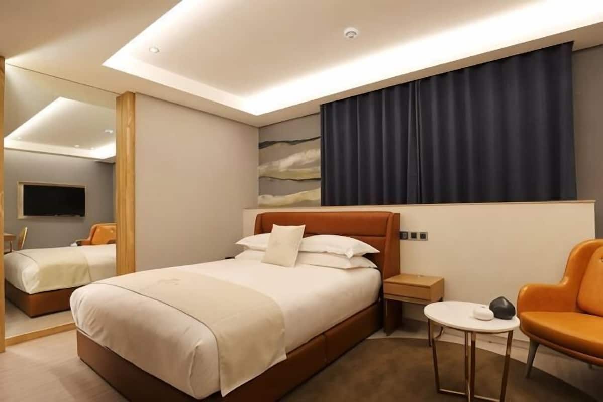 A hotel room with a large bed, a bedside table, a chair, a TV, and a painting on the wall.