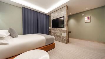 A hotel room with a bed, a flat-screen TV mounted on a marble wall, a large window with curtains, and a light-colored carpet.