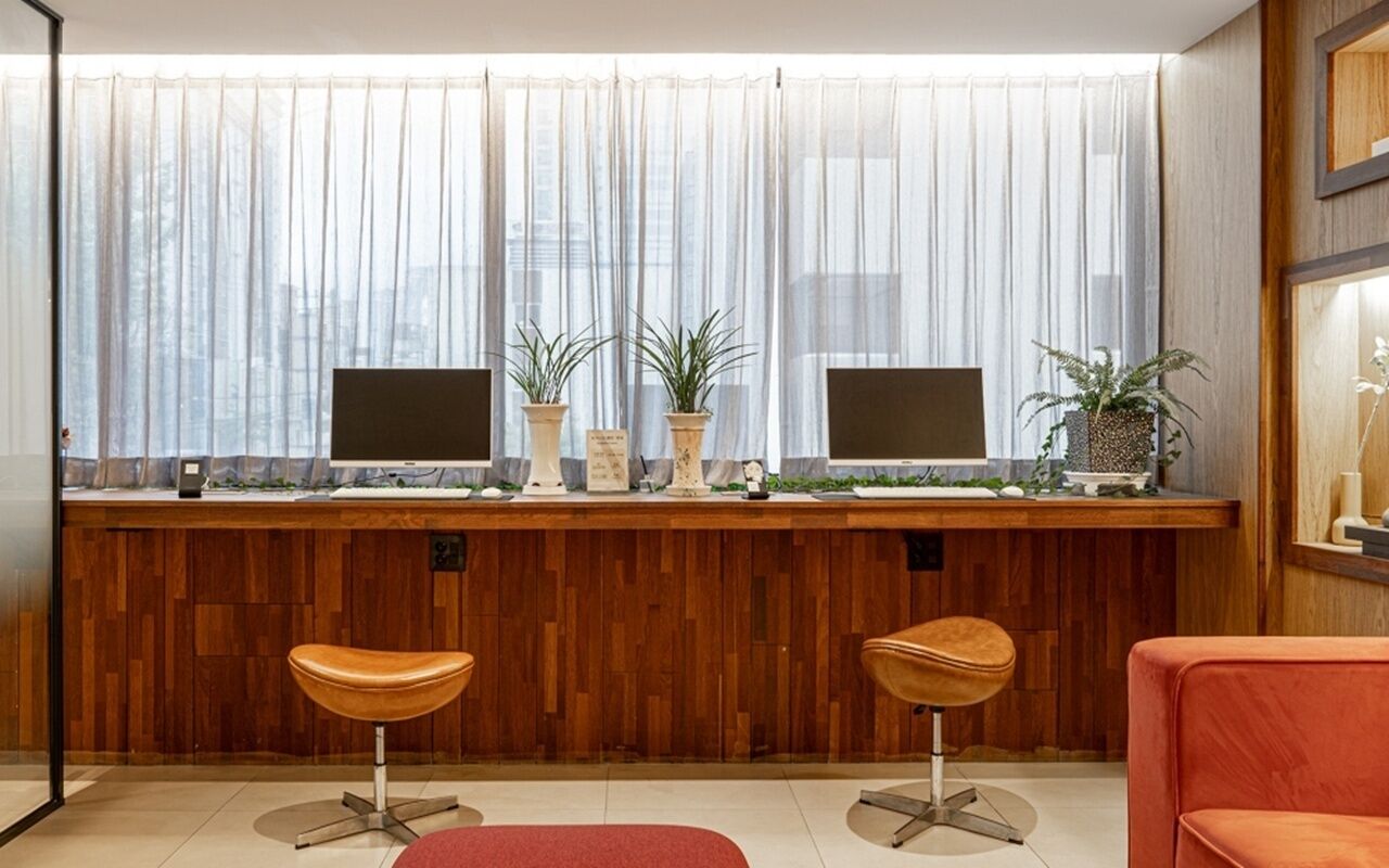 A reception area with a wooden counter, two monitors, potted plants, and two bar stools.