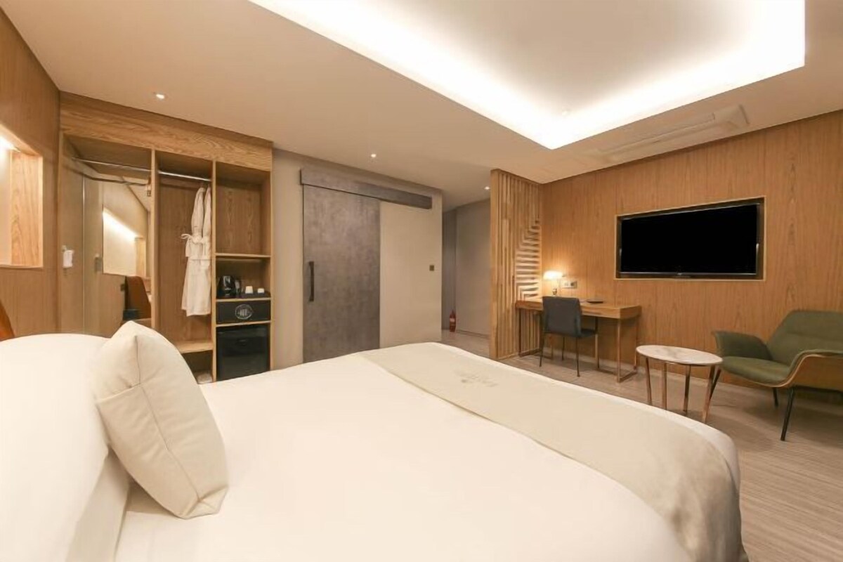 A hotel room with a bed, a desk, a chair, a TV, and a wardrobe.