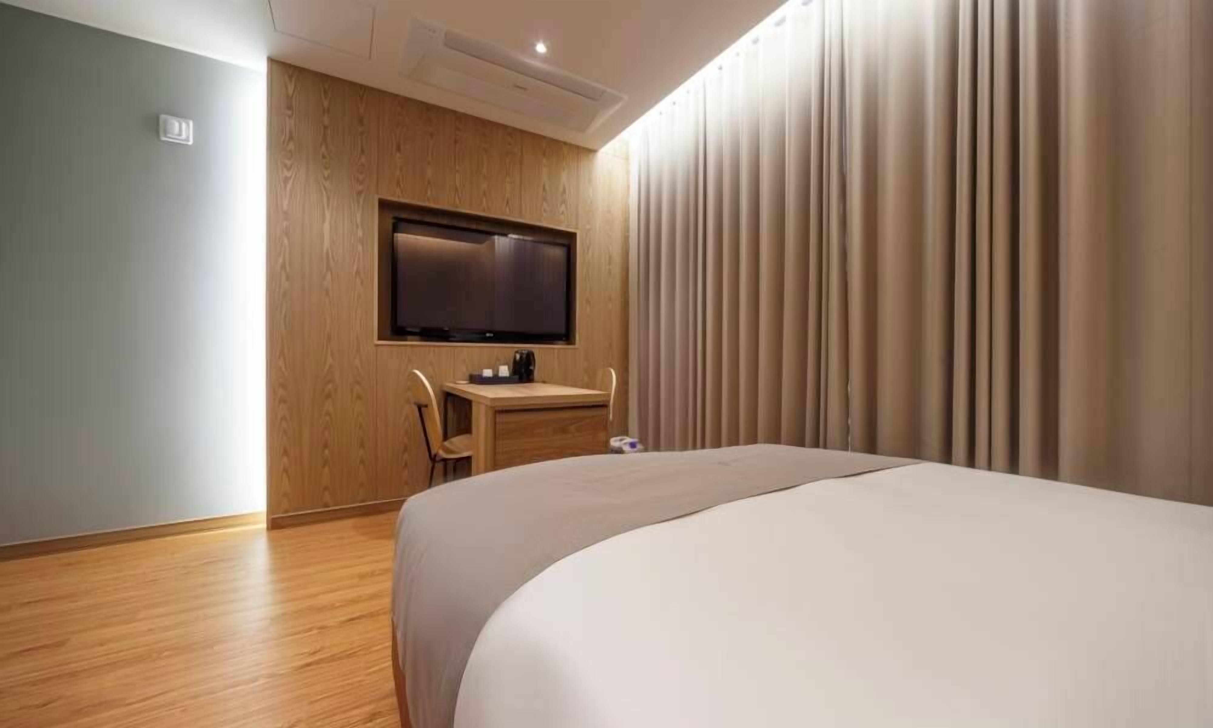 Een hotelkamer met een bed, een bureau, een stoel, een televisie en een gordijn.