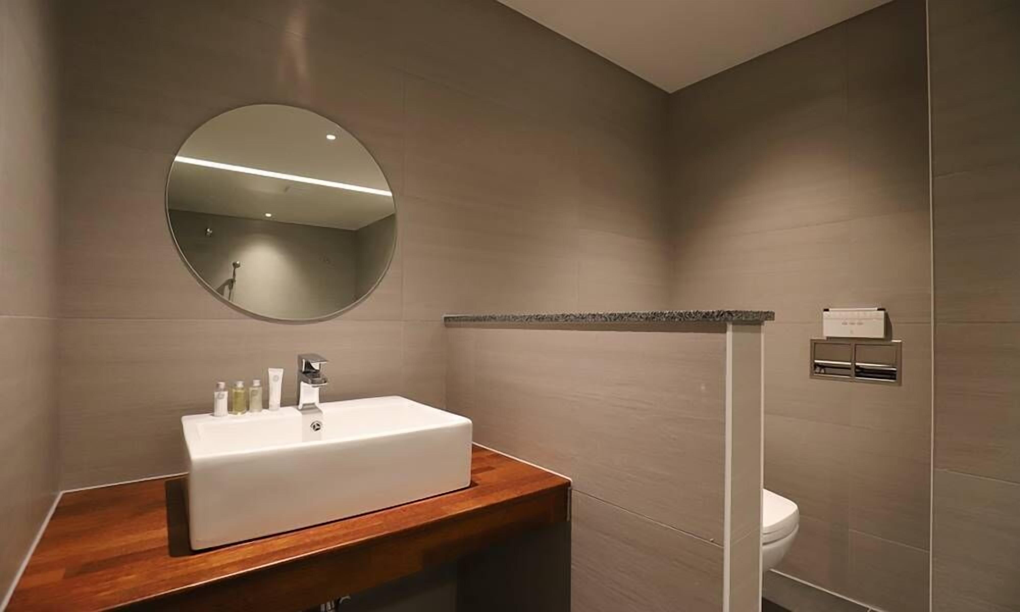 Un baño moderno con un lavamanos rectangular, un espejo redondo y un inodoro.