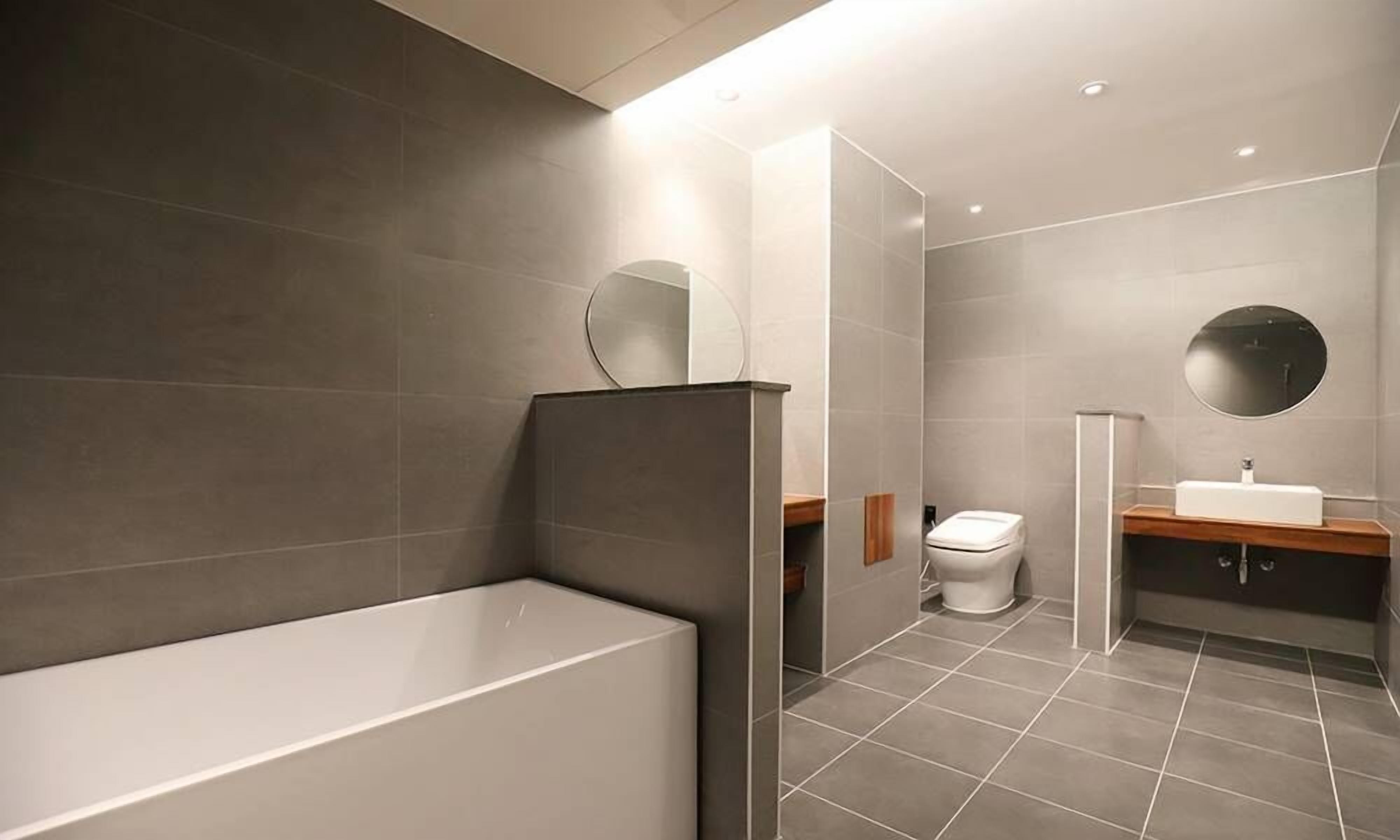 Un baño moderno con bañera, inodoro y lavamanos, que presenta baldosas grandes y un diseño minimalista.