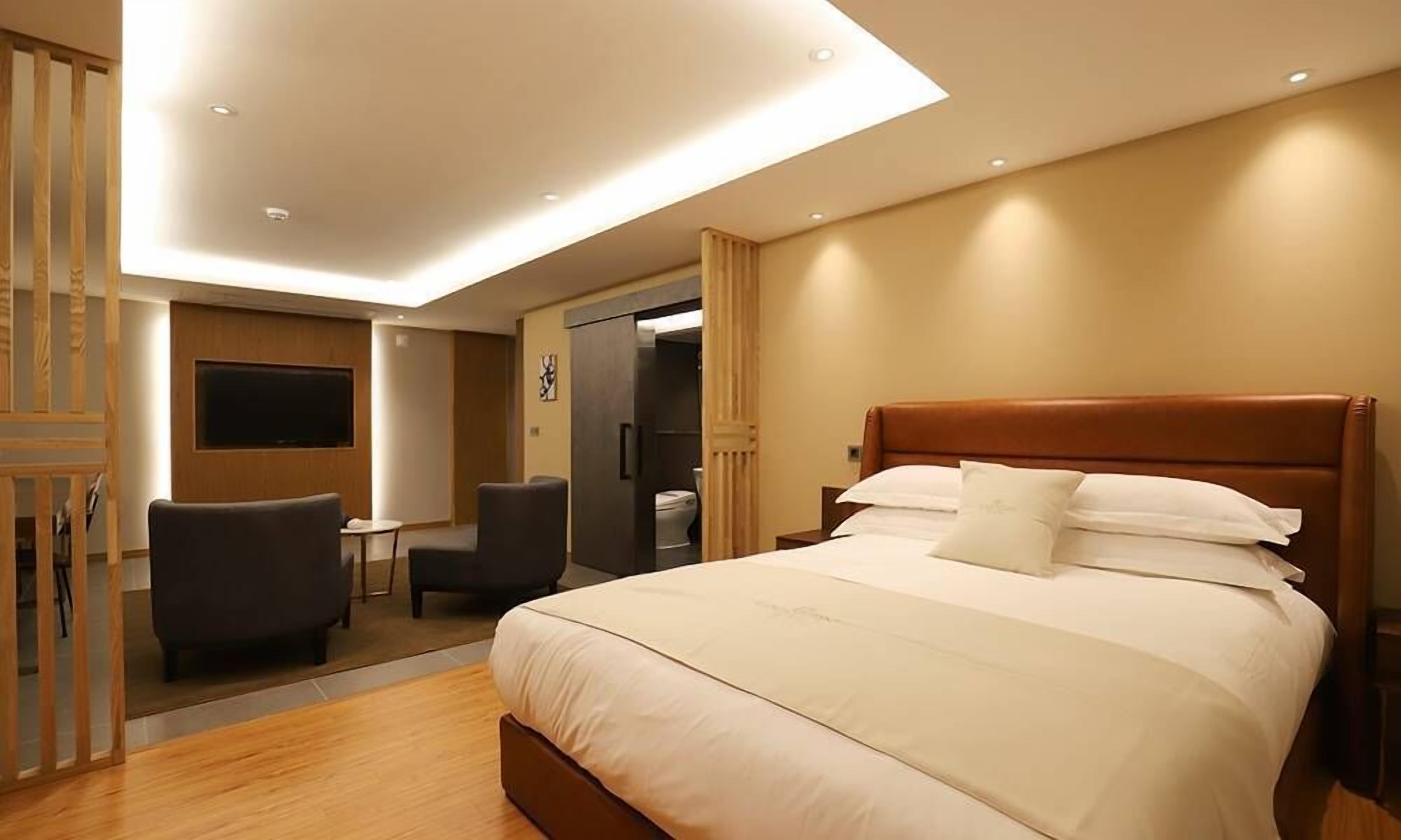 A modern hotel room with a large bed, a desk, two chairs, a TV, and a wardrobe.
