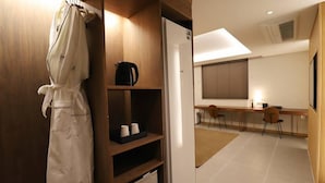 A hotel room with a wooden wardrobe, a robe hanging, a coffee maker, and a desk with chairs. - Dongdaegu Station Eastern Hotel (Daegu)