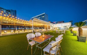 An outdoor seating area with tables and chairs, a covered walkway, and a building in the background. - Dongdaegu Station Eastern Hotel (Daegu)