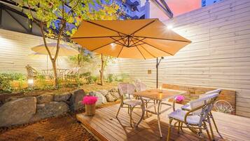Un patio al aire libre con cubierta de madera, mobiliario de mimbre y una gran sombrilla que da sombra.