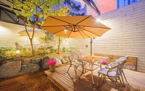 An outdoor patio with a wooden deck, wicker furniture, and a large umbrella providing shade. - Dongdaegu Station Eastern Hotel (Daegu)