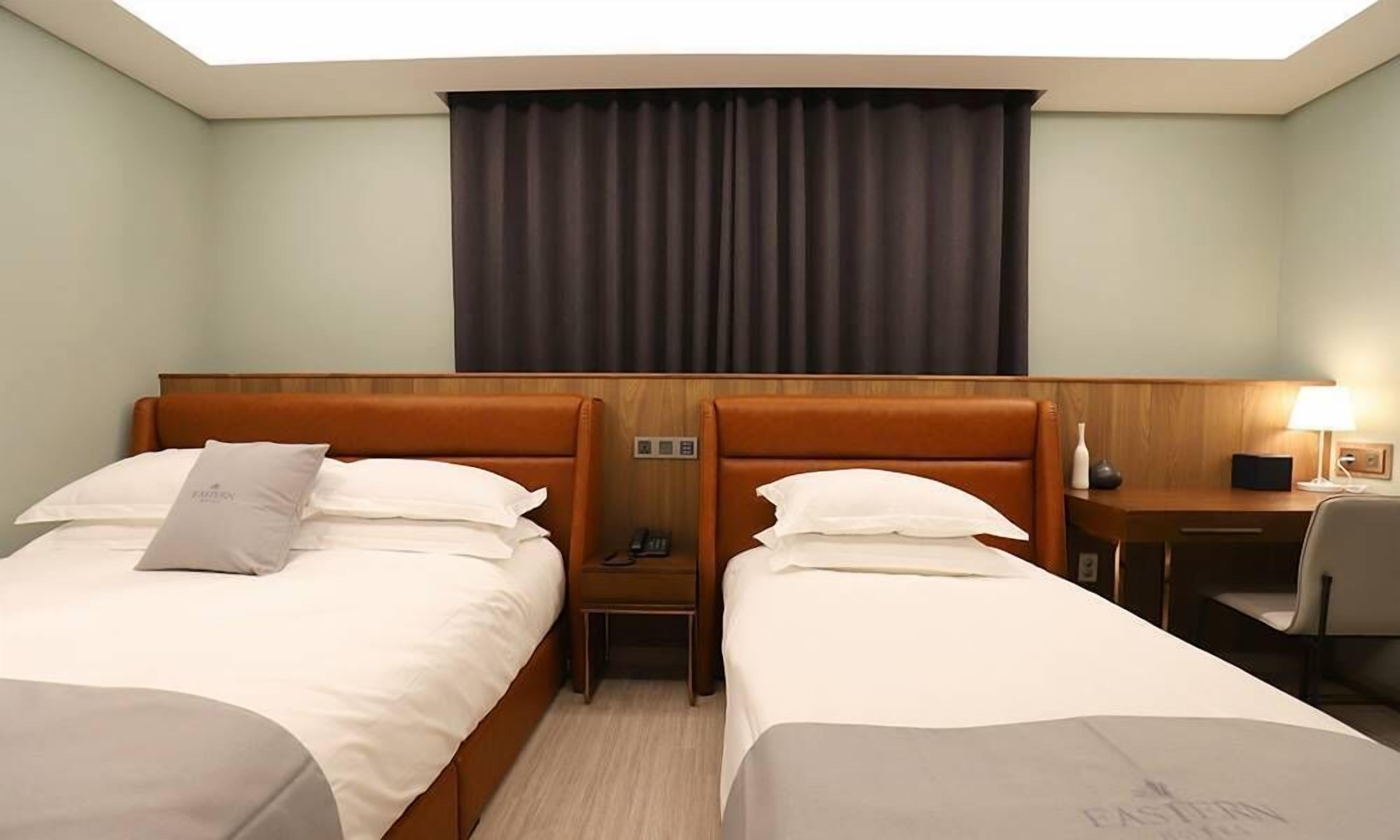 Habitación de hotel con dos camas, un escritorio, una silla, una lámpara y una ventana con cortinas.