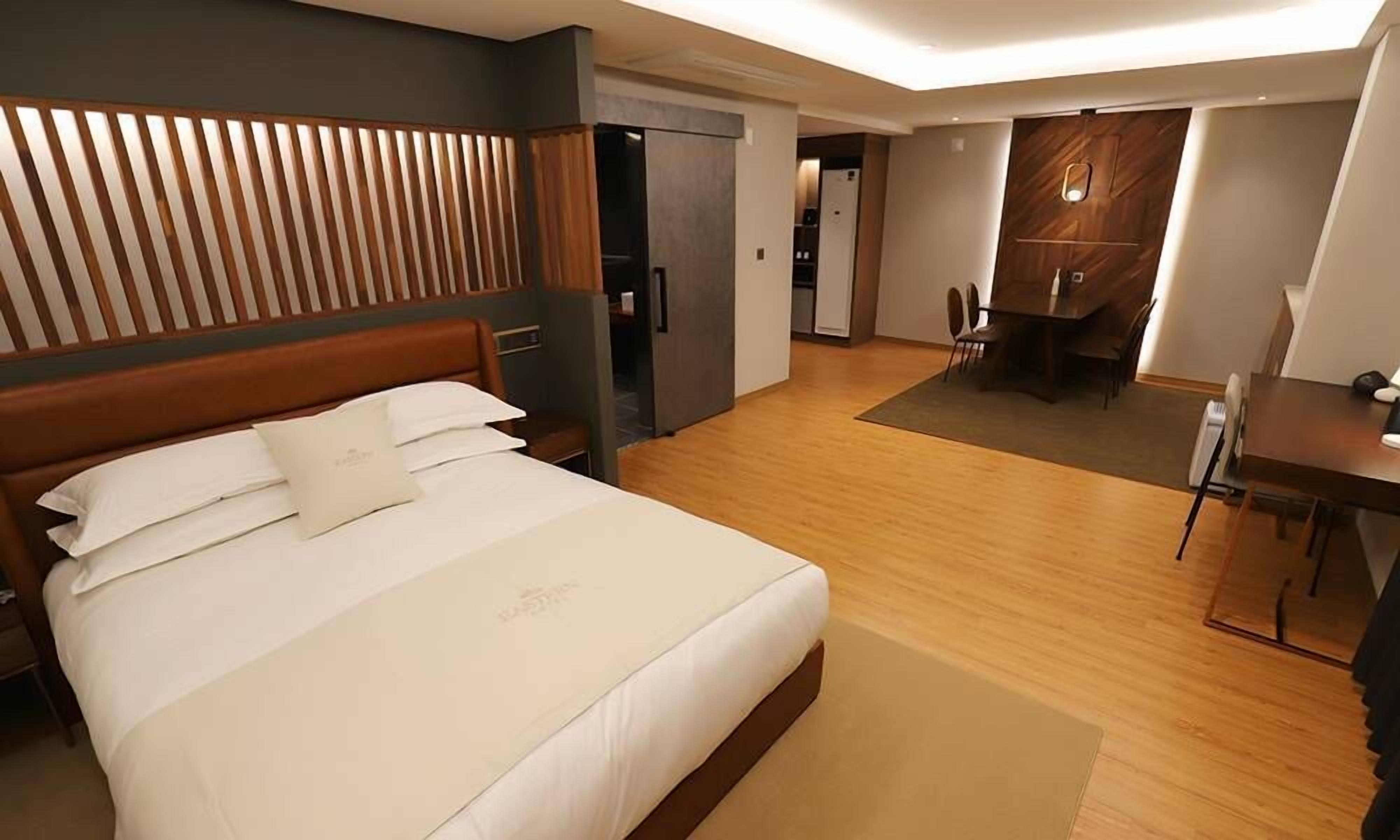 Una habitación de hotel con una cama grande, cabecera de madera, escritorio y zona de comedor.