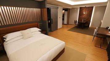Una habitación de hotel con una cama grande, cabecera de madera, escritorio y zona de comedor.