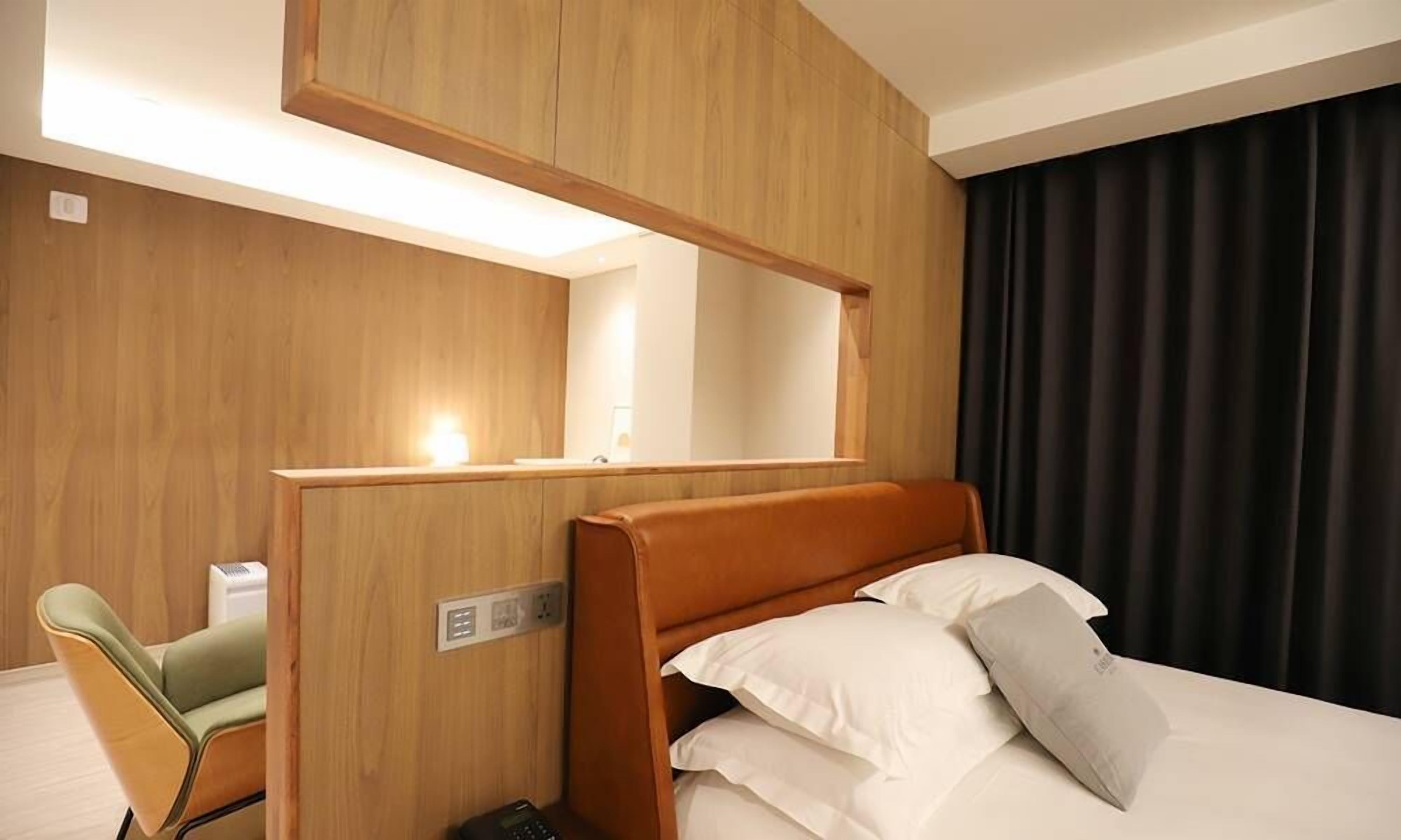 A hotel room with a bed, a desk, a chair, a mirror, and a window with curtains.