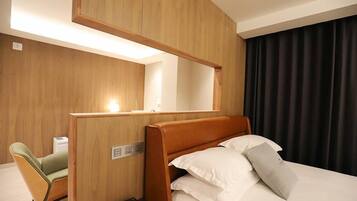 Una habitación de hotel con cama, escritorio, silla, espejo y ventana con cortinas.