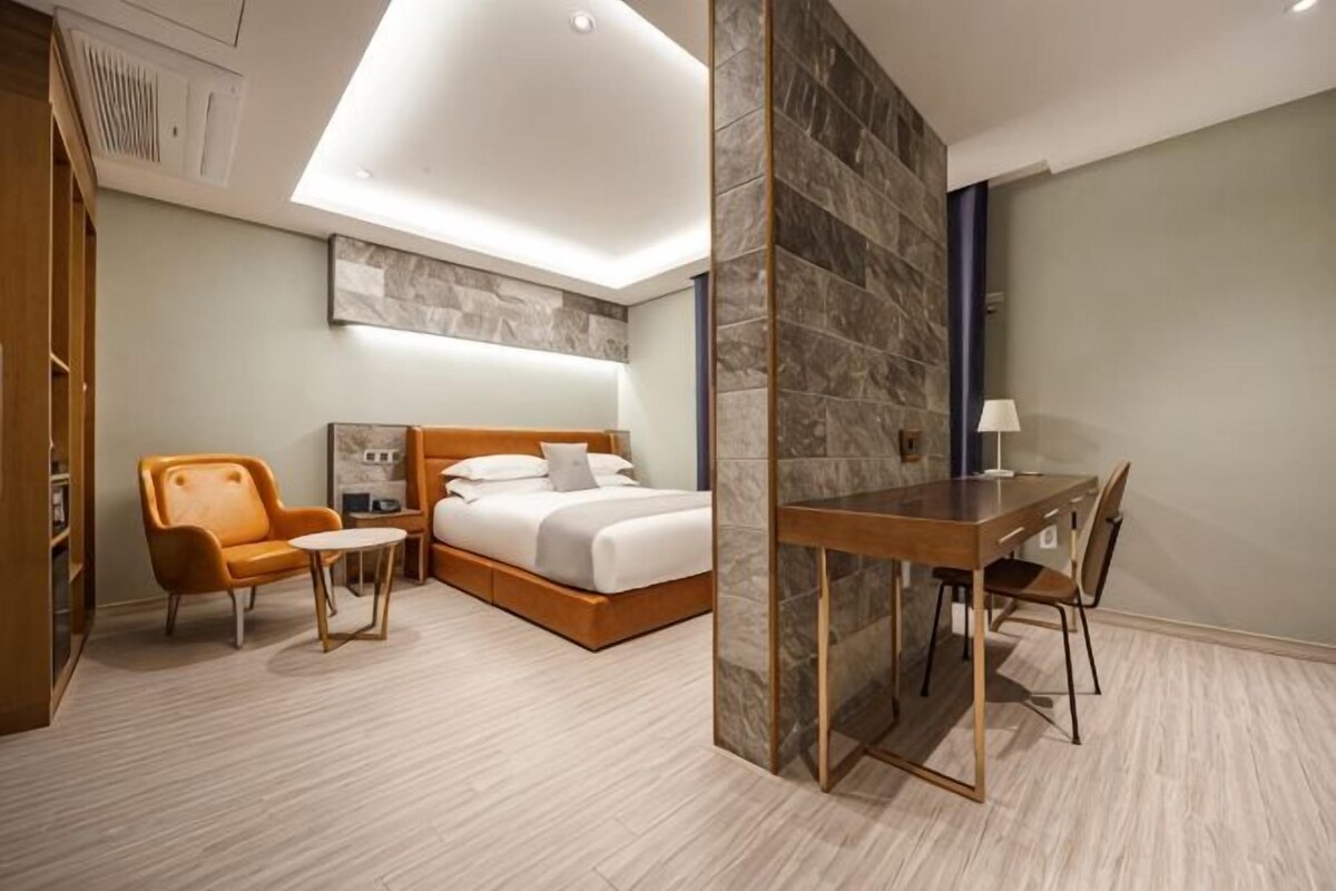 A hotel room with a bed, a desk, a chair, a small table, and a wardrobe.