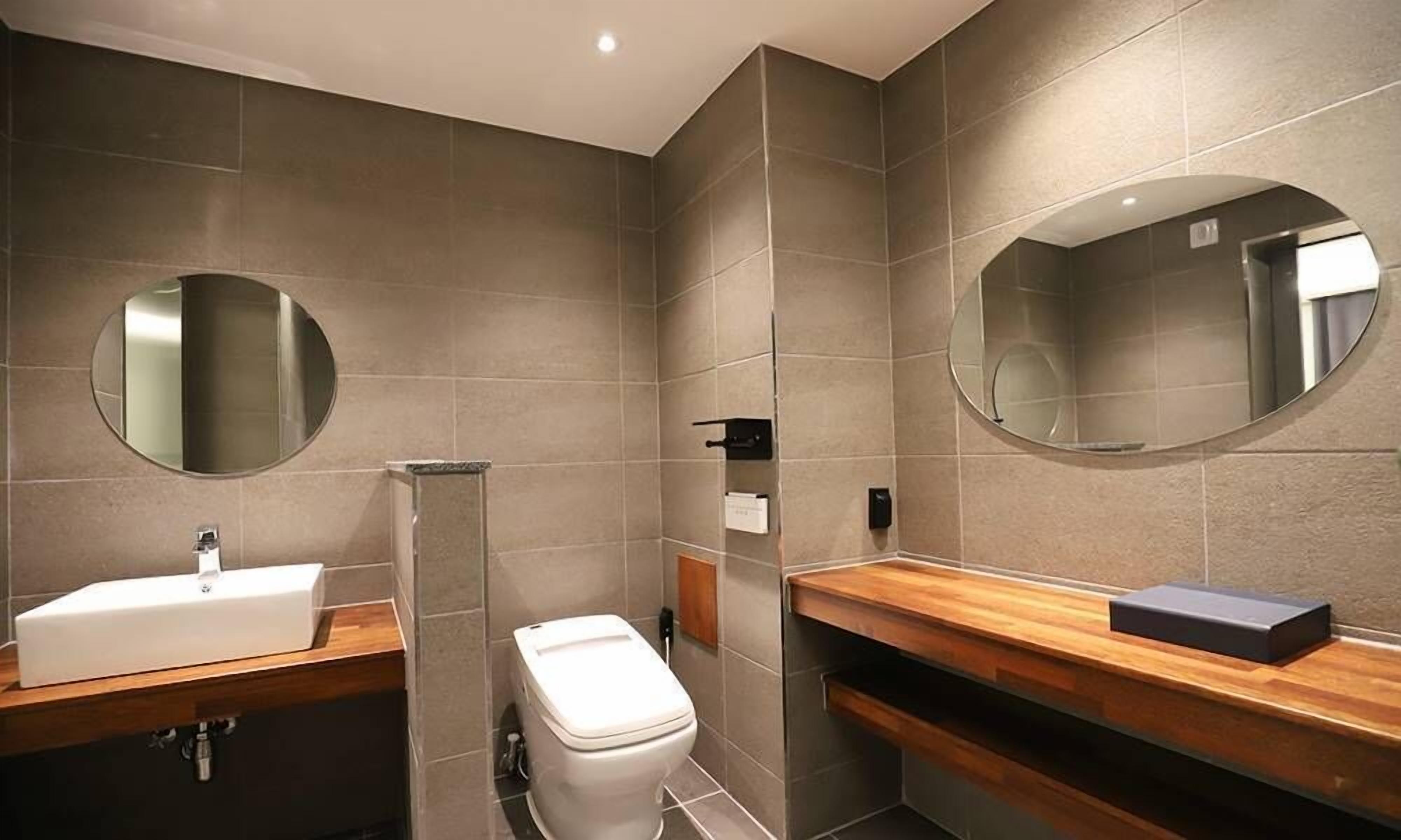A modern bathroom with a white sink, wooden vanity, a toilet, and two large mirrors.
