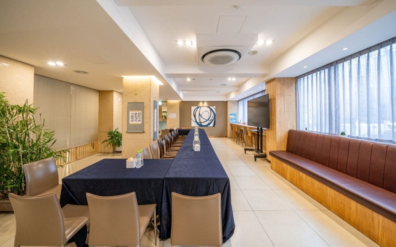 Una sala de conferencias con una mesa larga, sillas, un sofá y un amplio ventanal.