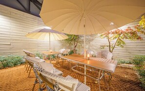 An outdoor patio with a wooden table and chairs, a large umbrella, and a small tree. - Dongdaegu Station Eastern Hotel (Daegu)