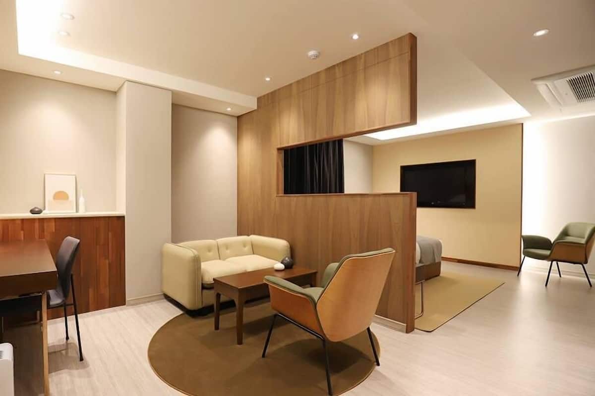 A modern hotel room with a wooden partition, a sofa, a dining table, and a TV.