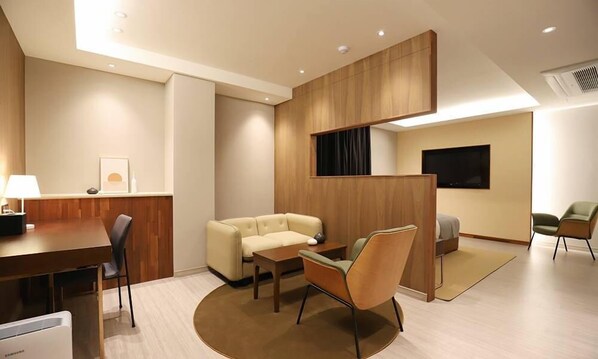 A modern hotel room with a wooden partition, a sofa, a dining table, and a TV.