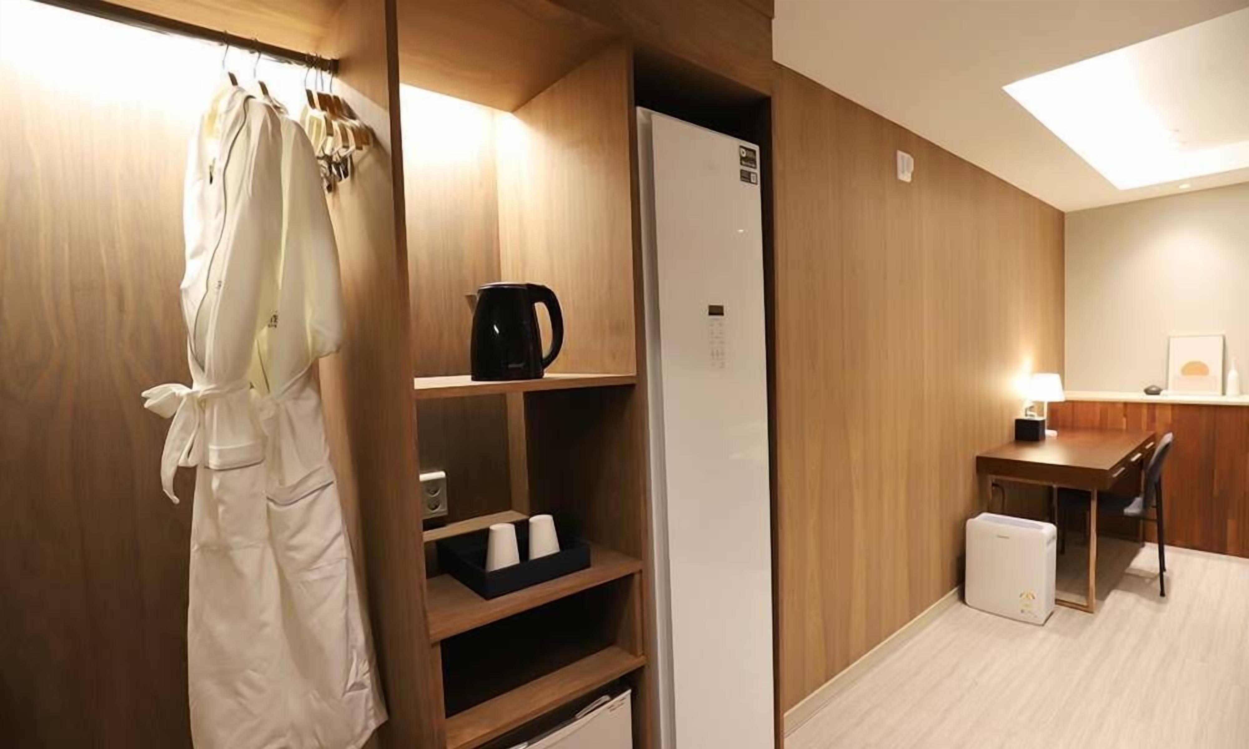 Habitació d'hotel amb un armari de fusta, una cuineta petita, un escriptori amb una làmpada i un llit.