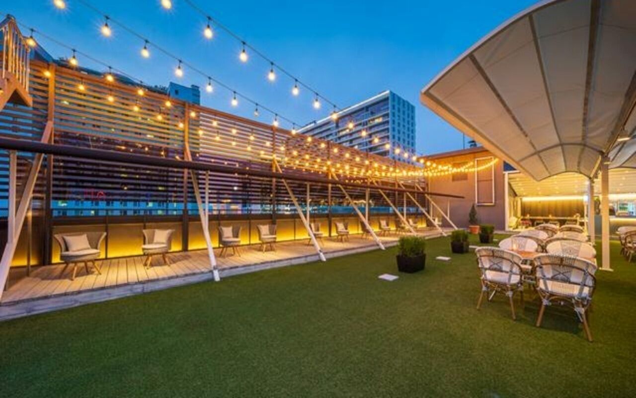 An outdoor seating area with string lights, a covered section, and a grassy lawn.