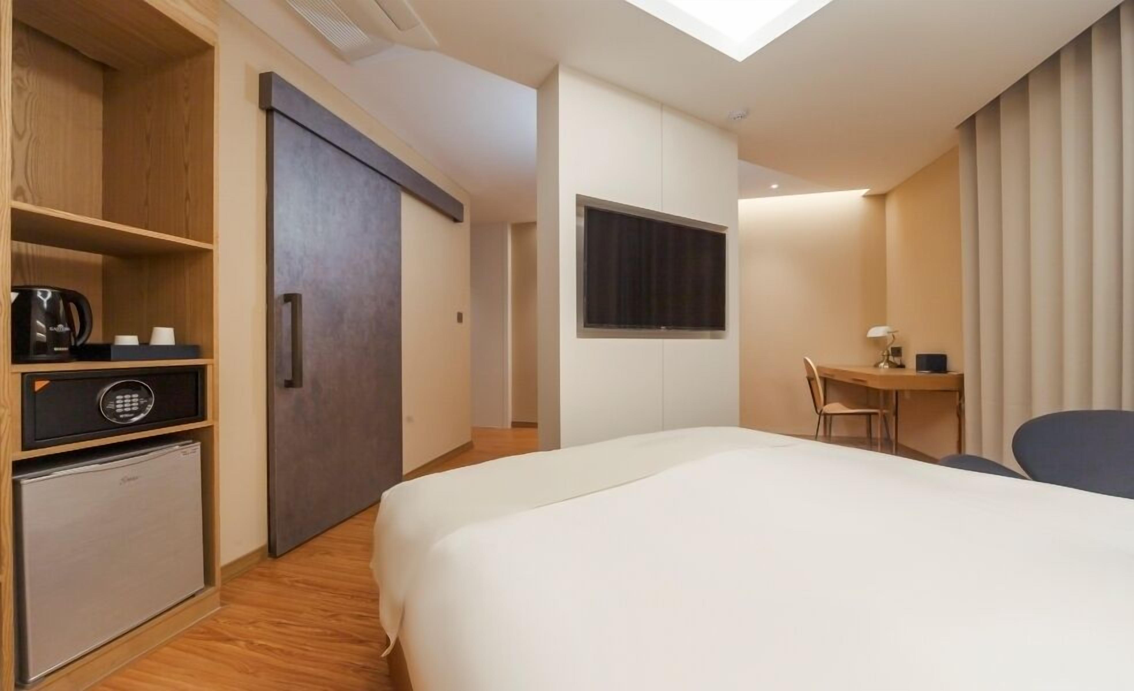 Una habitación de hotel moderna con cama, escritorio, silla, refrigerador pequeño y armario.