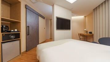 Una habitación de hotel moderna con cama, escritorio, silla, refrigerador pequeño y armario.