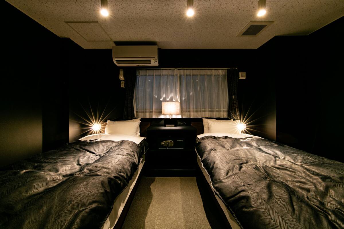 A hotel room with two beds, a nightstand, a lamp, and an air conditioning unit.
