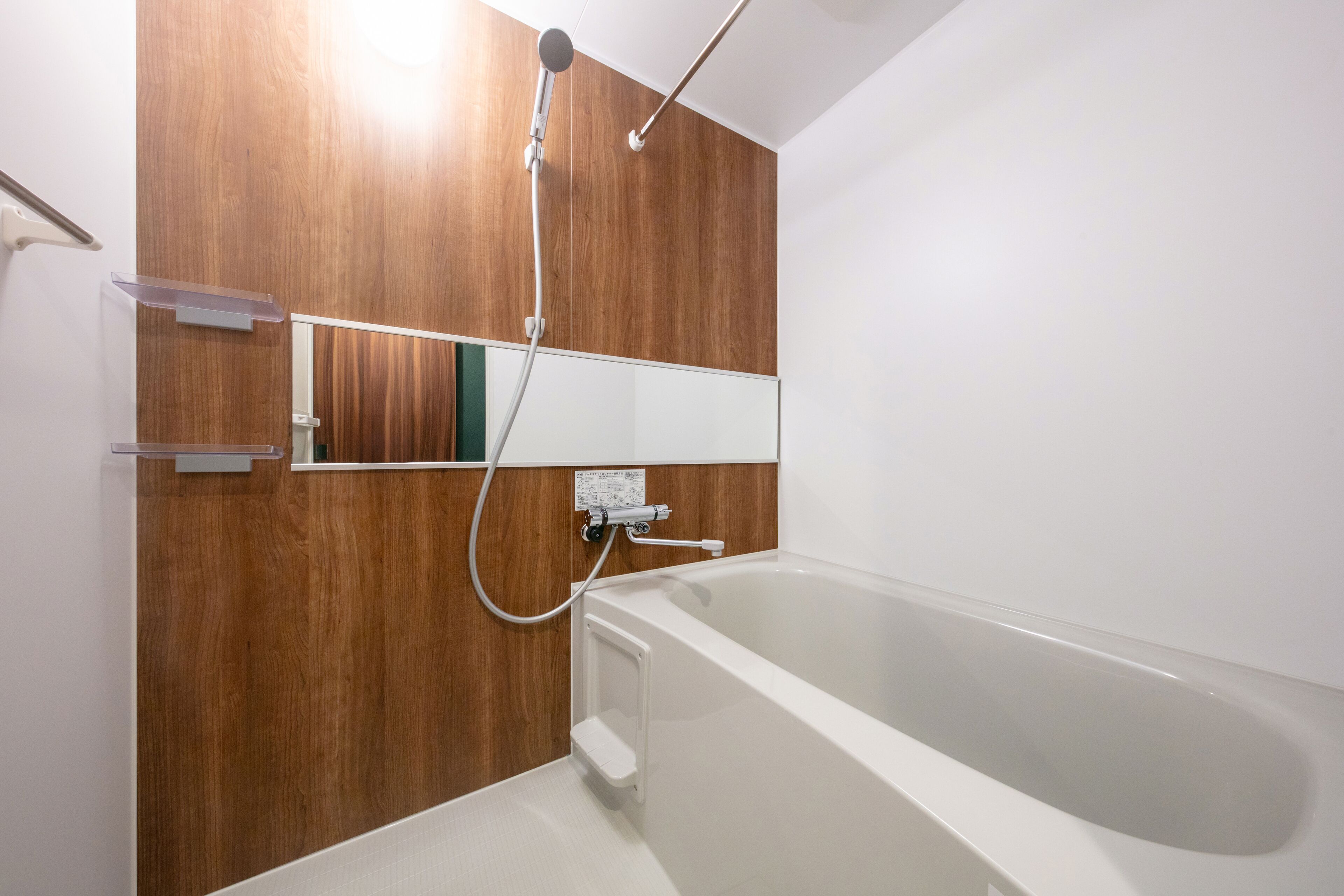A modern bathroom with a wooden wall panel, a white bathtub, and a mounted mirror.