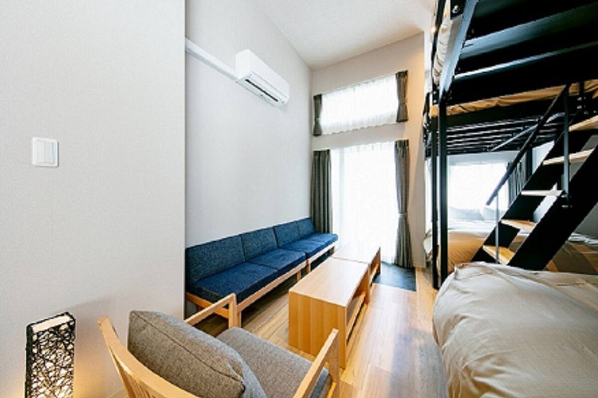 A compact hotel room with bunk beds, a sofa, a small table, and a window with curtains.