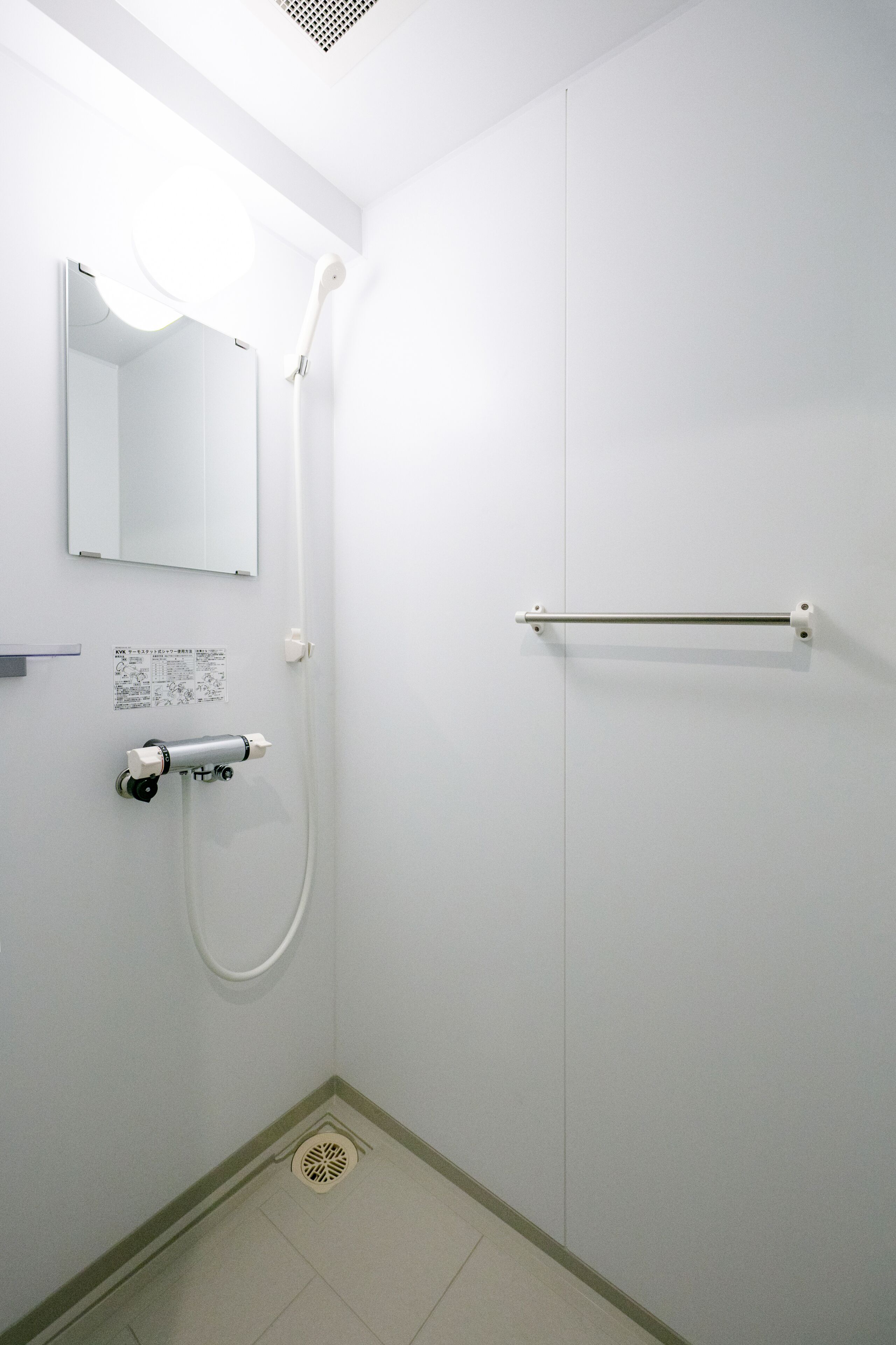 A small, white bathroom with a shower, a toilet, and a hand dryer.