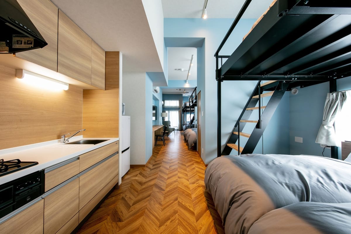 A compact, modern apartment with a kitchenette, a bed, and a staircase leading to an upper level.