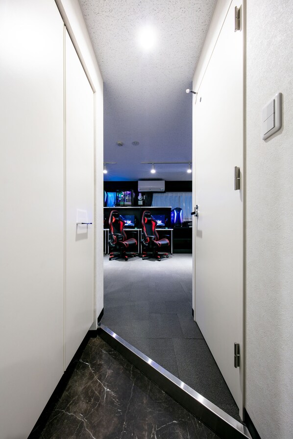 A hallway leading to a gaming room with two gaming chairs, a desk, and a large screen.
