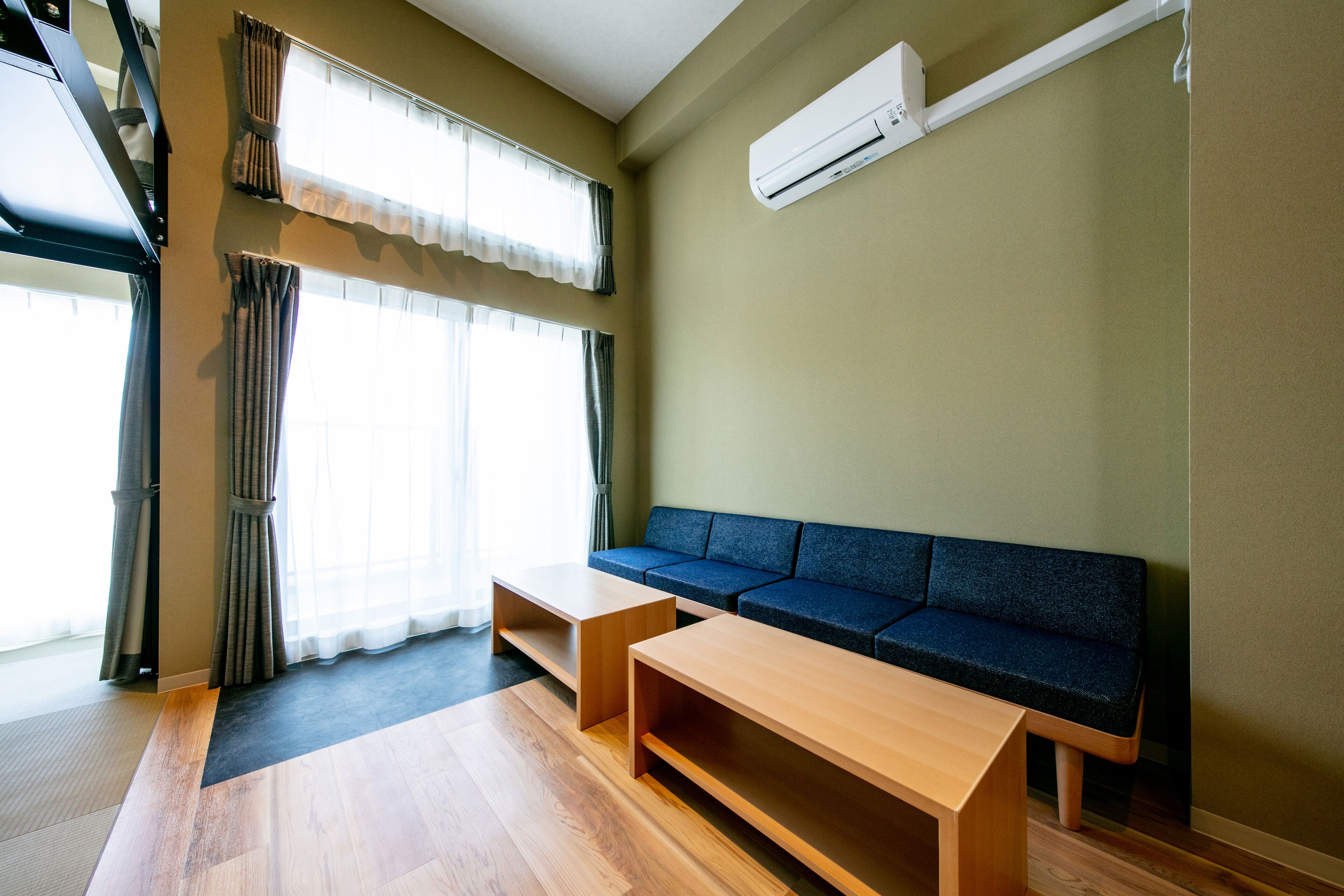 A modern living room with a sofa, two wooden tables, and a large window with curtains.