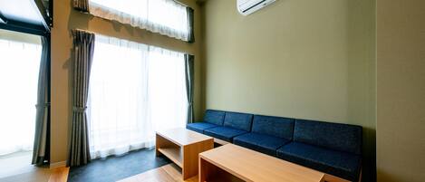 A modern living room with a sofa, two wooden tables, and a large window with curtains.