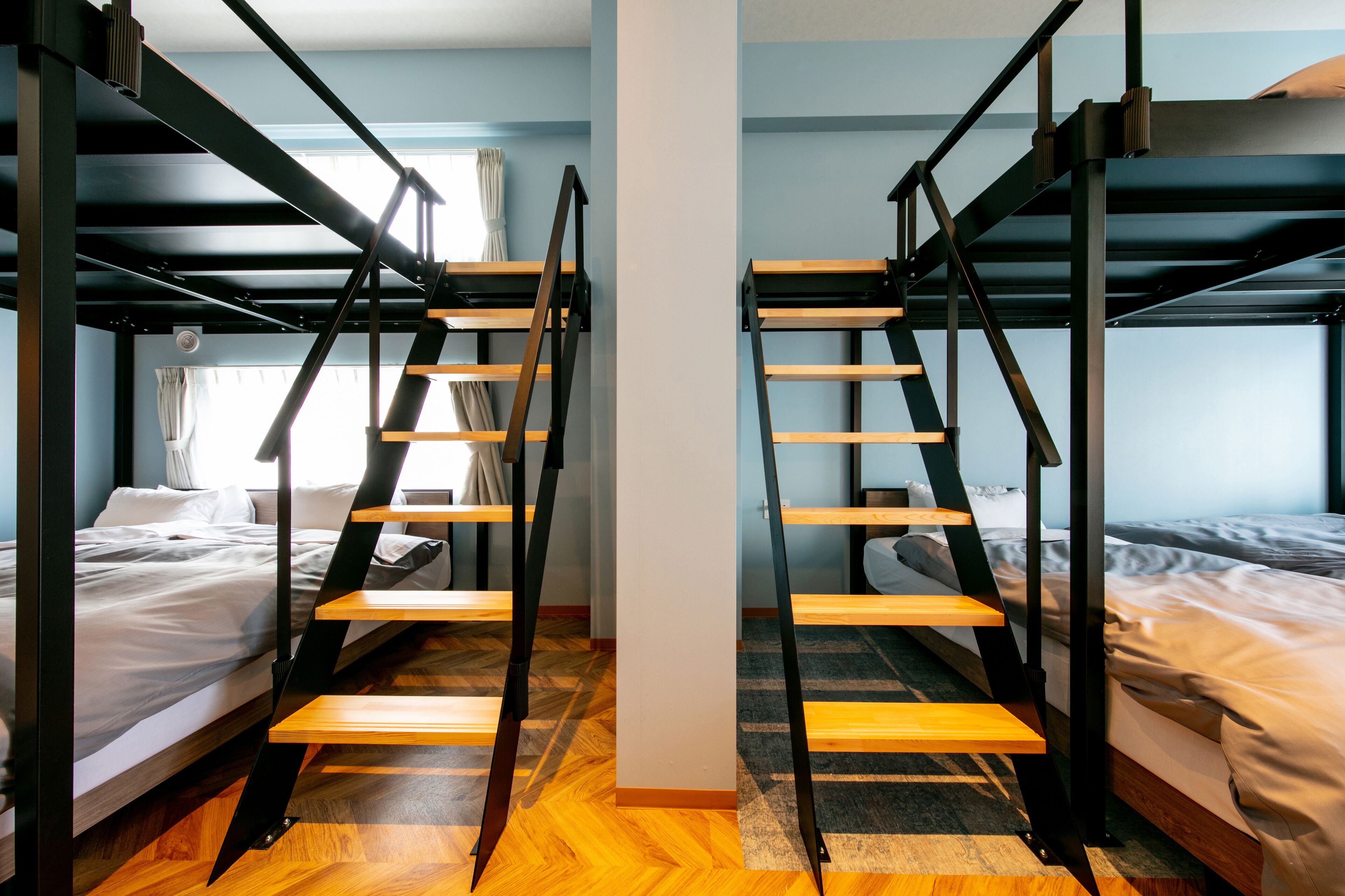 A room with bunk beds, wooden ladders, and a window with curtains.