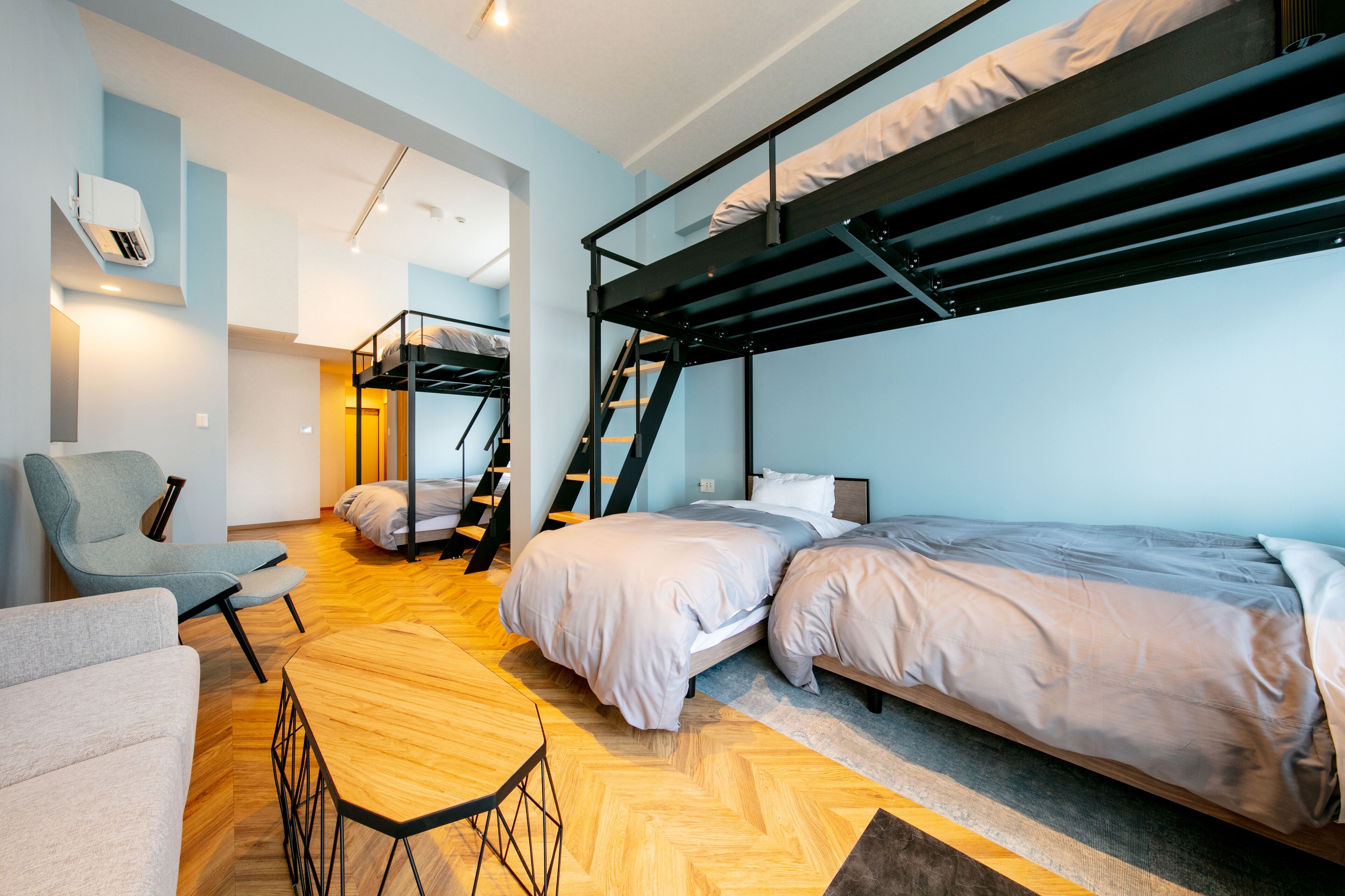 Habitación compacta y moderna con literas, una silla, una mesita y una escalera que conduce a un nivel superior.