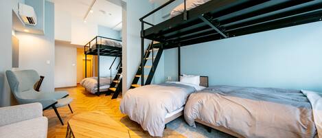 Habitación compacta y moderna con literas, una silla, una mesita y una escalera que conduce a un nivel superior.