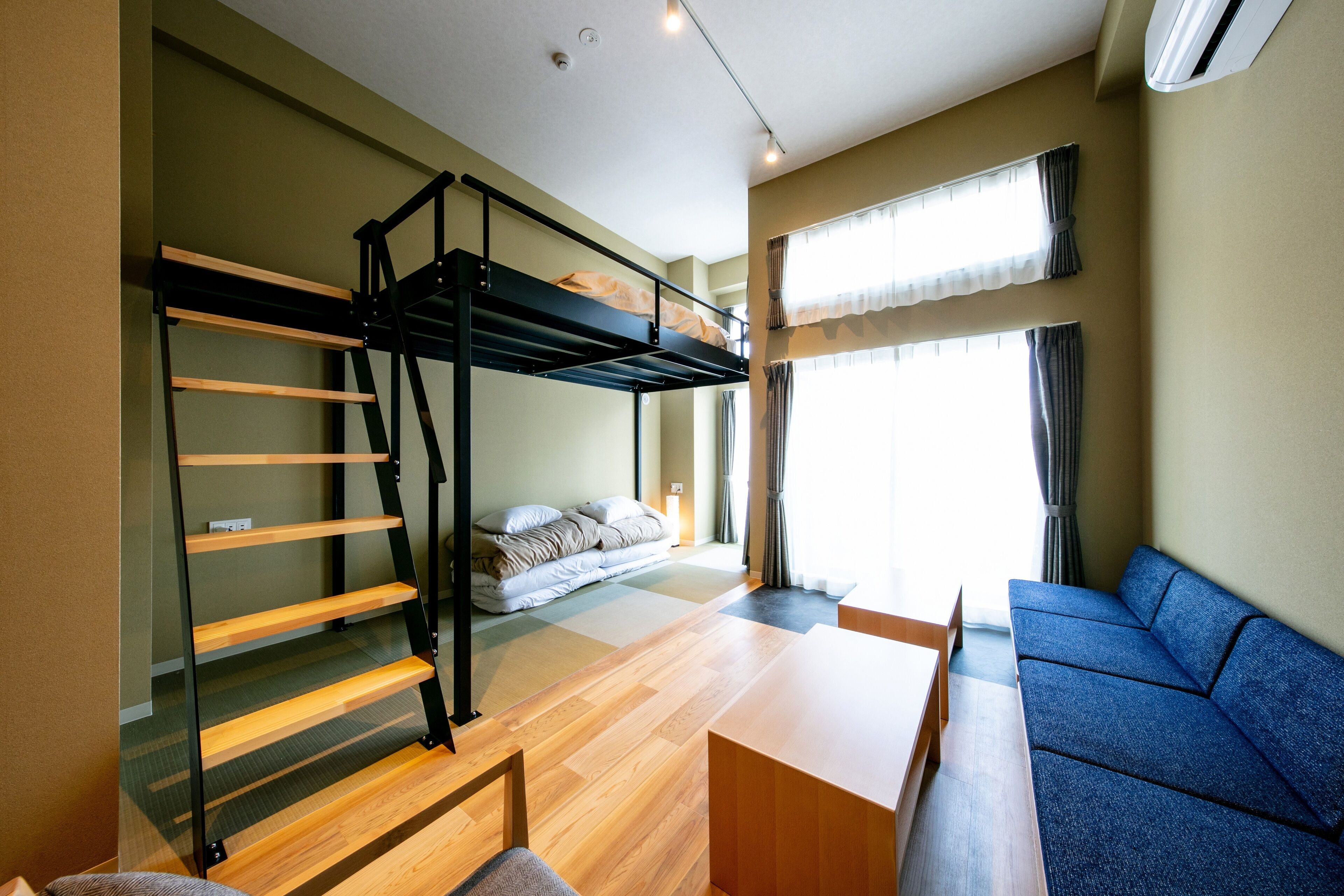 A compact room with a bunk bed, a sofa, a dining table, and a large window.