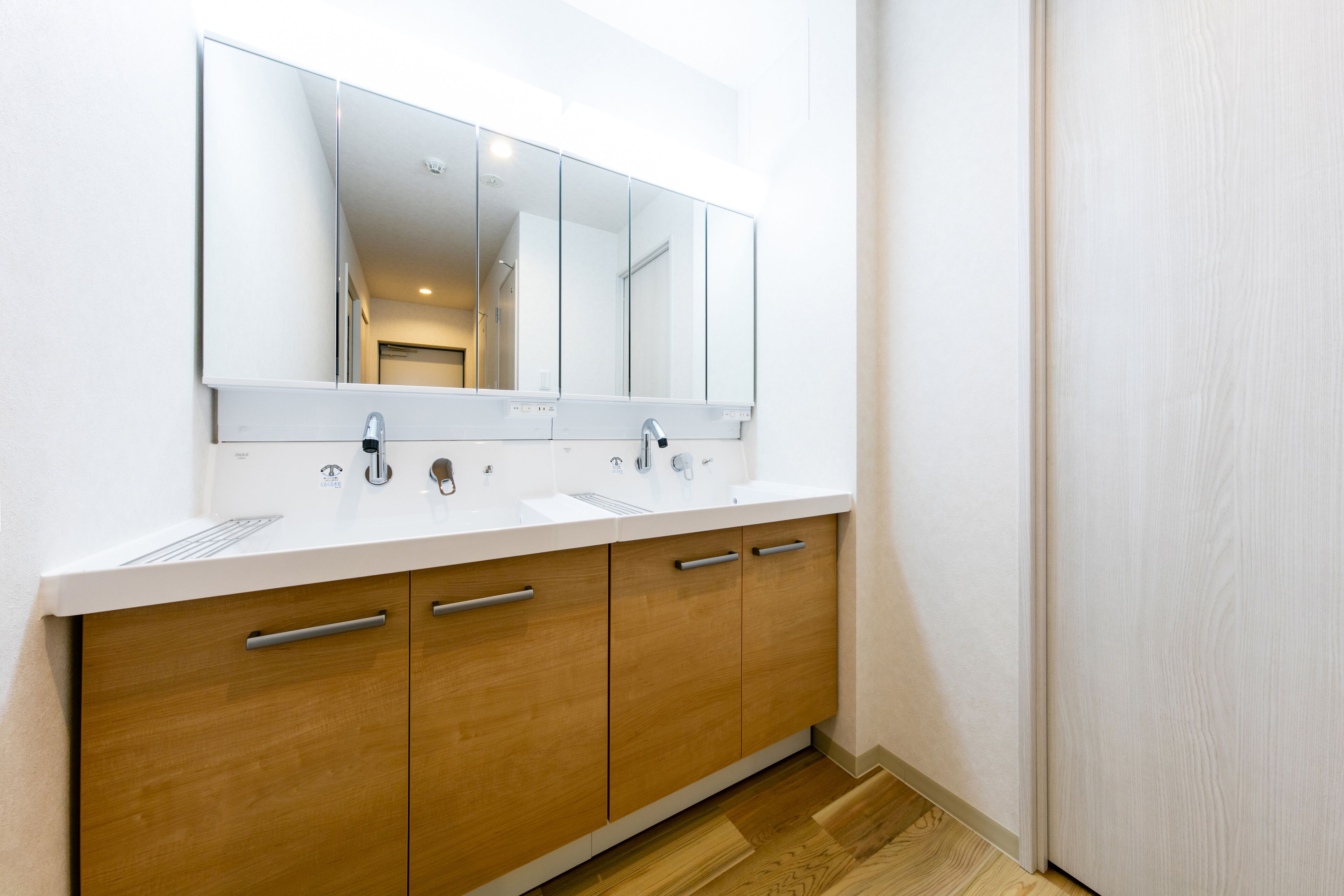 A modern bathroom with a large mirror, two sinks, wooden cabinets, and a white countertop.