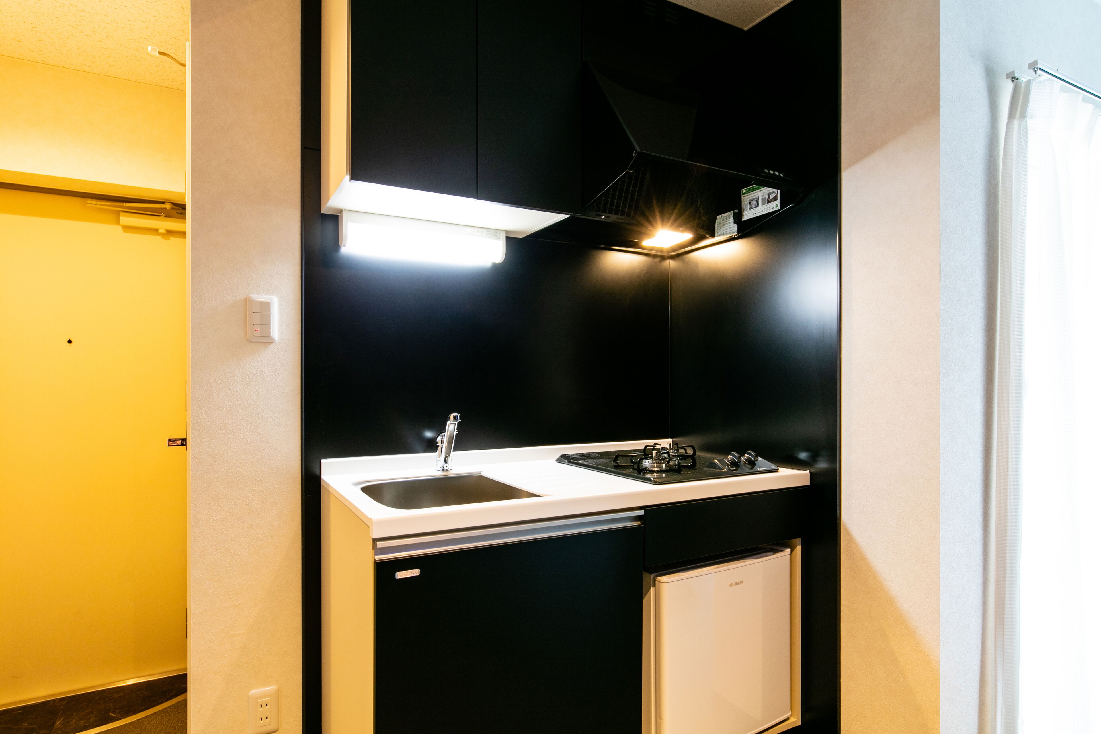Une cuisine compacte dotée d’un plan de travail blanc, de meubles noirs, d’un lave-vaisselle encastré et d’un petit réfrigérateur.