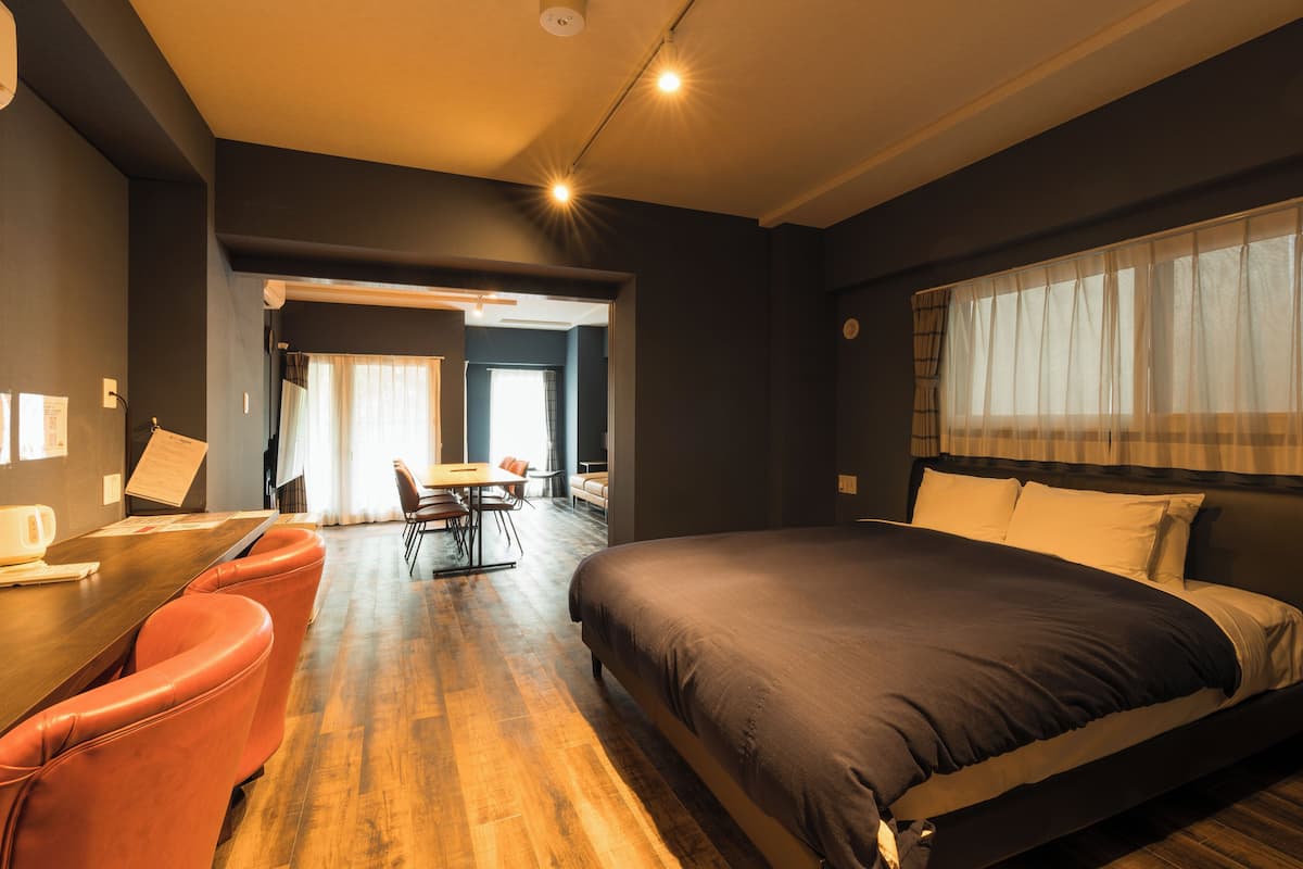 A modern hotel room with a large bed, a wooden dining table, and orange chairs.