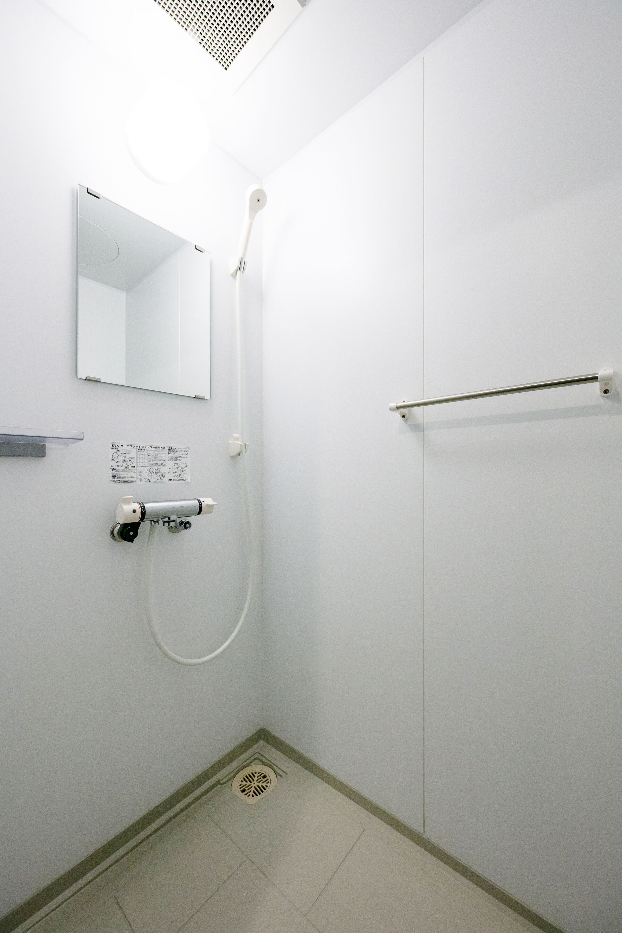 A small, white bathroom with a shower, a toilet, and a mirror.