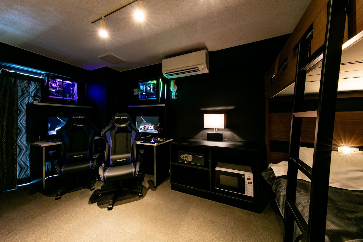 A gaming room with two gaming chairs, a desk with a computer, and a bed with bunk beds.