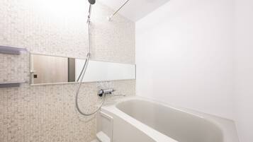 Un baño moderno con una bañera independiente, un cabezal de ducha manual y un espejo instalado en la pared.